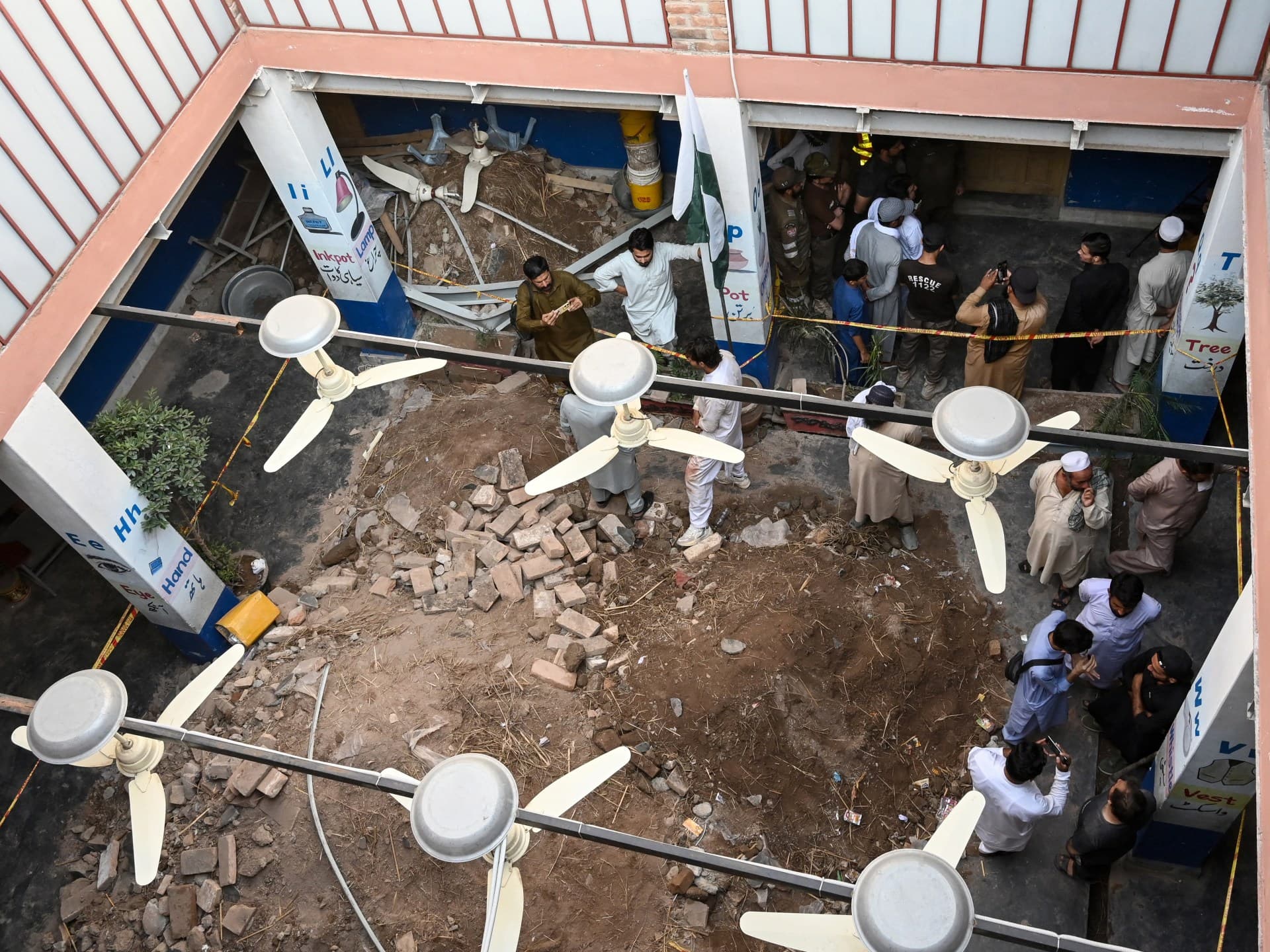 People gather around debris and rubble in the courtyard of the Al-Khair Education Centre following the roof collapse in Peshawar on 15 October.
