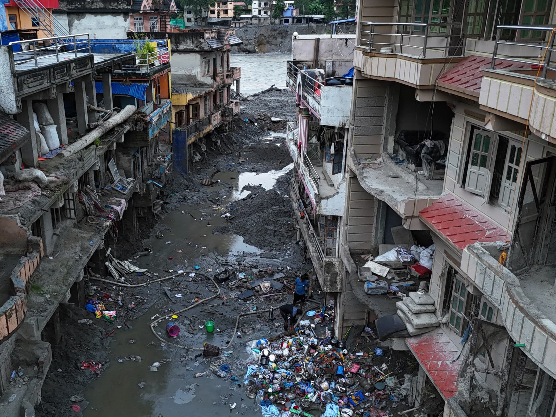 People salvage items from sludge on September 26, 2026, next to deluged houses in Nepal’s Nuwakot district in the aftermath of last month’s flash flooding.