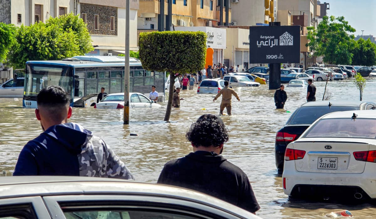 People walk near stalled vehicles along a flooded street following heavy rains in Tripoli on 13 October.