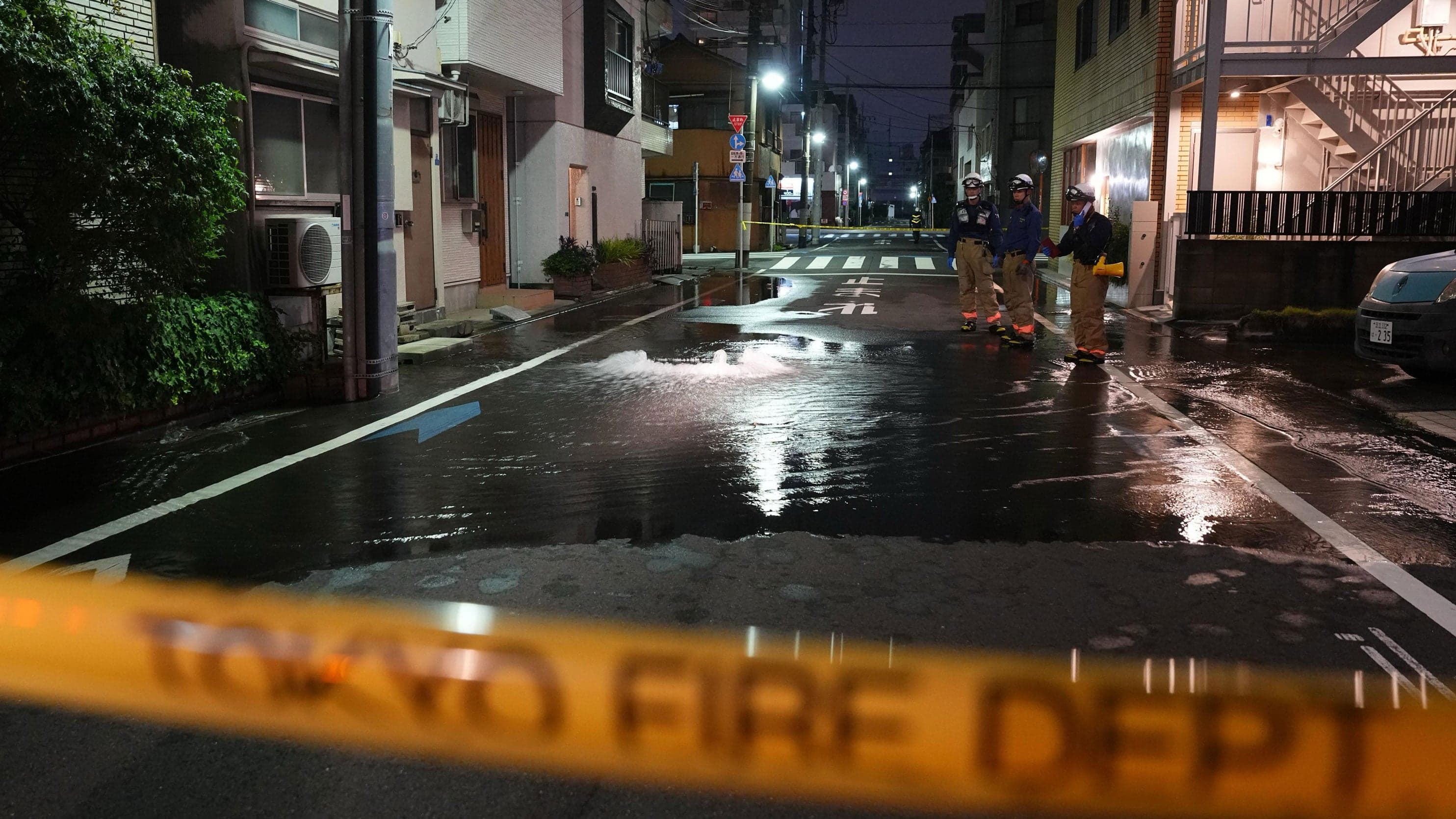 First responders from the Tokyo Fire Department stand on a street partially flooded in the early hours of Sunday, Aug. 23, 2026, following the rupture of a water pipe after an…